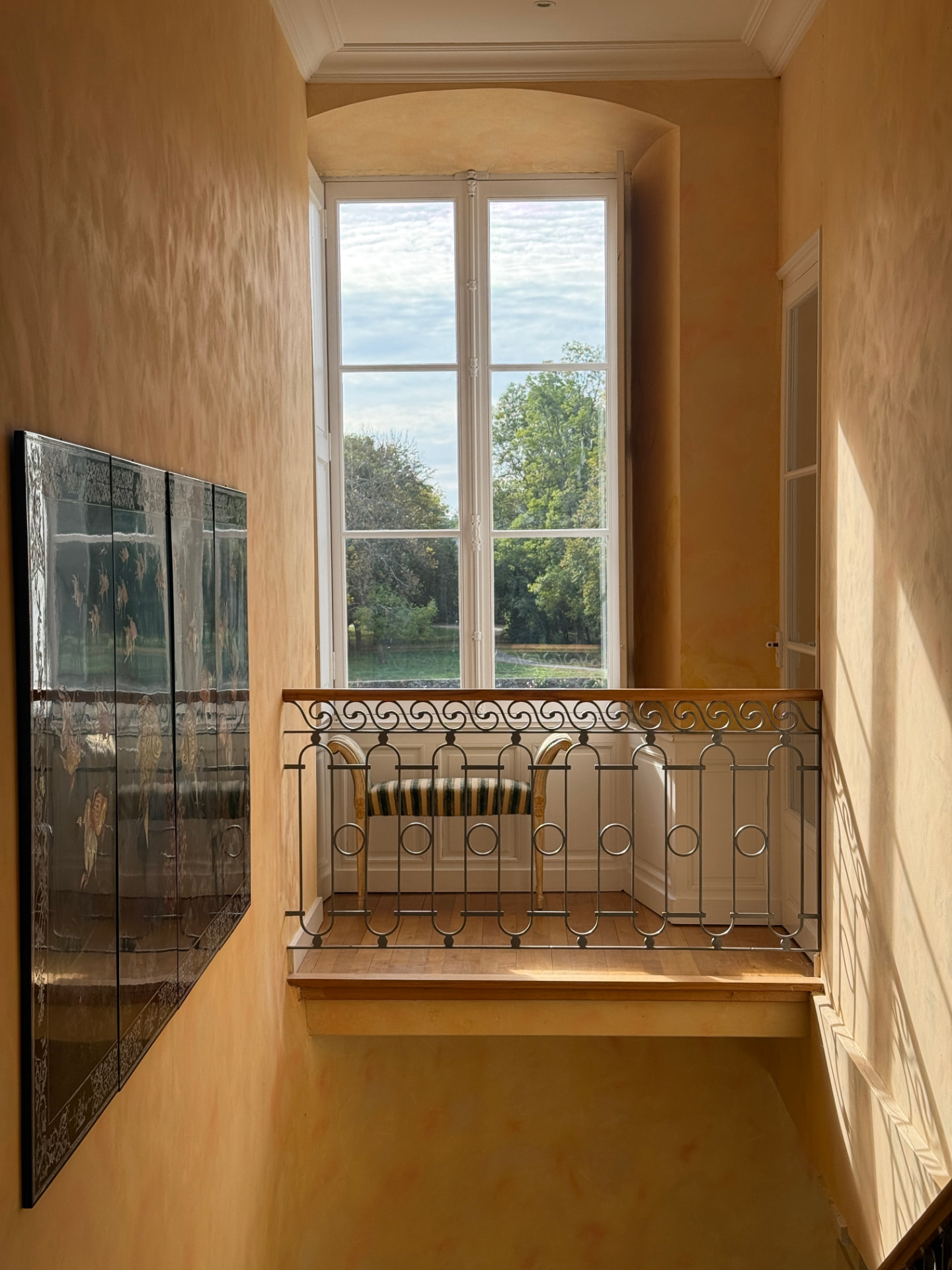 The stair landing — lacquered screen, wrought-iron rail, window to the park
