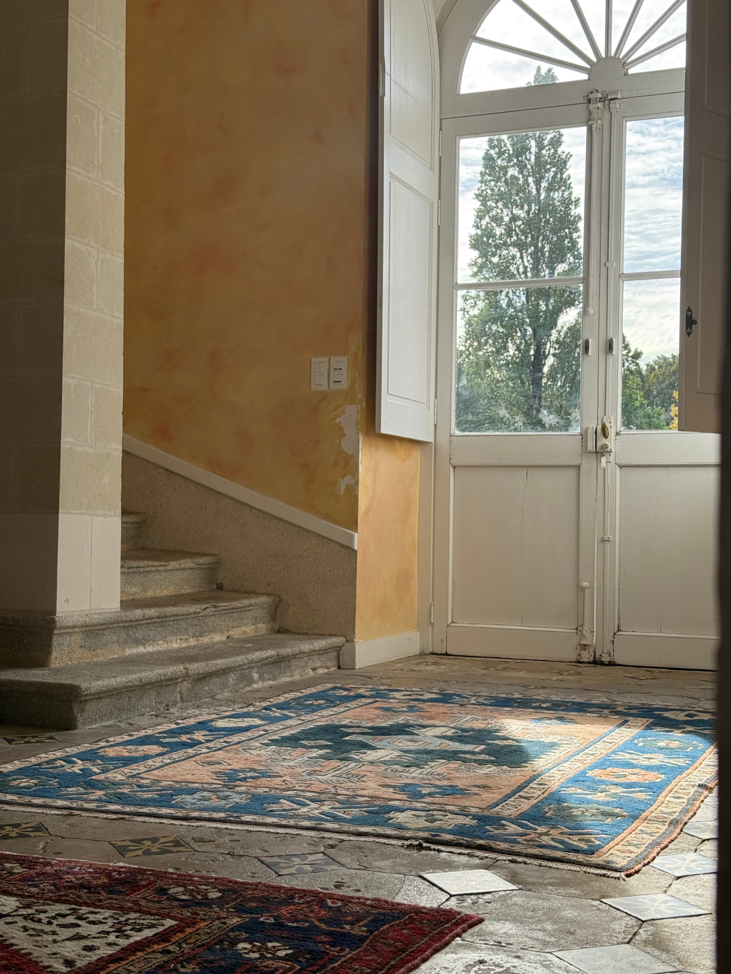 The entrance hall — stone stair, French doors open to the park